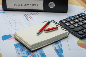 Segregator z dokumentami, kalkulator i papiery z danymi finansowymi, wykresami i analizami leżą na biurku - obrazy, fototapety, plakaty