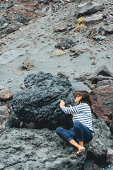 person touching massive volcanic rock from mountain in island