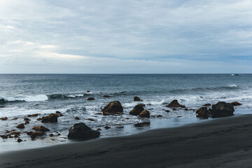 Fototapeta na wymiar view of moody dark sand beach with many rocks hit by the furious ocean 