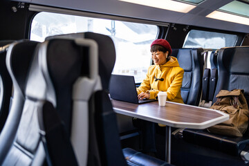 First class train interior and woman working on lap top computer while traveling. - obrazy, fototapety, plakaty
