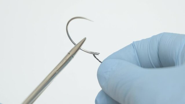 Male doctor's hands in strike gloves extend the thread into a curved surgical needle, suture material
