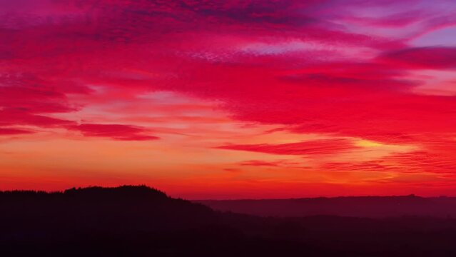Tracking aerial telephoto shot of landscape under intense red sunset sky