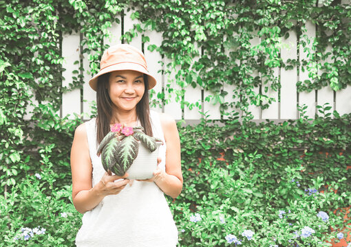 Asian  cheerful female gardener standing in the garden holding pot with Carpet Plant. Concept of hobby, homegrowing and leisure time