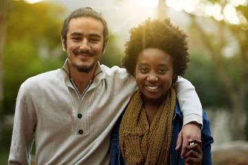  Park, portrait and happy interracial couple together with trees, sunshine and morning embrace with love. Romance, smile and date in nature, man and woman hug with diversity, connection and care. © peopleimages.com