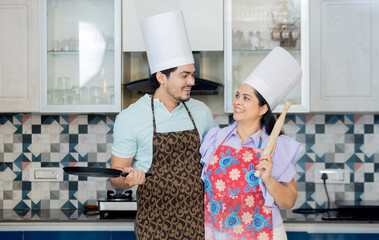 Happy indian couple dressed in cook uniform wearing a apron , chef hat ready to make tasty food....