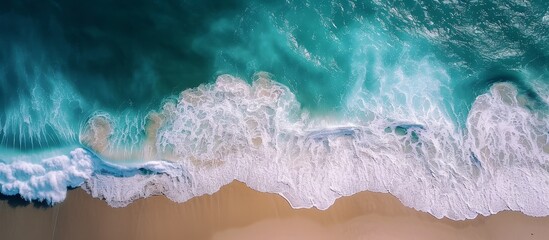 An artistic display of electric blue waves crashing on a sandy beach, witnessed from an aerial view. The sky, adorned with cumulus clouds, adds to the beauty of this meteorological phenomenon.