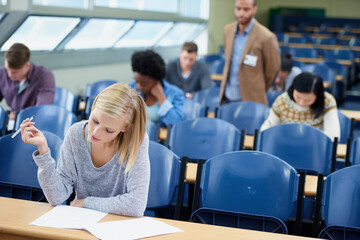 Exam, classroom and student with pen for thinking, assessment and writing at campus. Woman,...