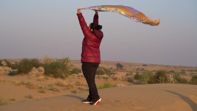 slow motion shot of young indian woman holding traditional chunni scarf over head flying in the wind at Sam sand dunes thar desert Jaisalmer rajasthan India