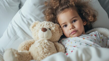 Young girl with curly hair resting her head on a white teddy bear both lying on a white pillow.