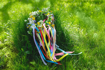 Spring flower wreath with colorful ribbons on grass in garden. floral decor. Symbol of Beltane, Wiccan Celtic Holiday beginning of summer. wheel of the year. pagan traditions, magic witch rituals - obrazy, fototapety, plakaty
