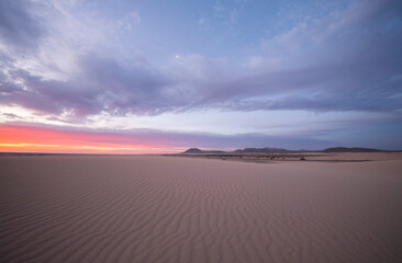 Salida del sol en medio de las Dunas de Corralejo con las dunas creadas en la arena blanca y el cielo teñido de colores rosados en la salida del sol, Fuerteventura, Canarias