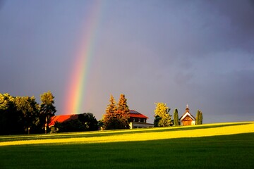 Regenbogen über dem leuchtend blauen Himmel und gelb grünes Gras vor der Schindelbergkapelle in...