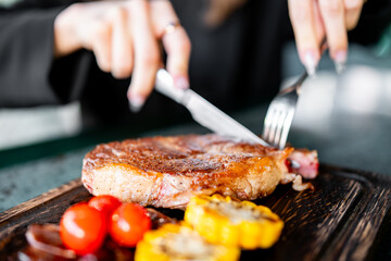 woman hands with fork and knife eating beef steak in cafe