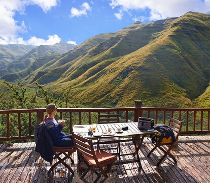 Woman, nature and eating on a balcony for holiday, vacation and travel destination at a countryside hotel or lodge. Person with breakfast, food and thinking of mountains or view on eco friendly patio