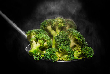 Fresh broccoli in spoon with steam on black background
