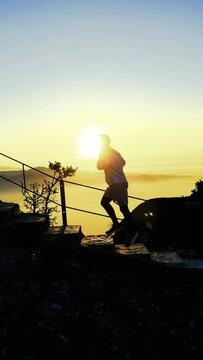 Silueta de deportista ascendiendo monta&ntilde;a con escalones al amanecer con la salida del sol detr&aacute;s por encima de las nubes. Video drone vertical 4k.
