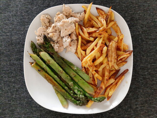 Homemade grilled chicken with french fries and grilled asparagus, served on a white plate
