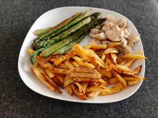 Homemade grilled chicken with french fries and grilled asparagus, served on a white plate