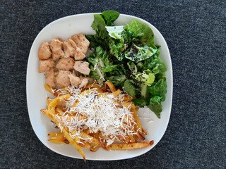 Homemade grilled chicken with french fries, cheese and green salad, served on a white plate