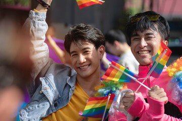 Two gay men join in the fun at the Pride parade, waving flags in celebration of Pride Month, LGBTQ...