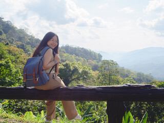 Asian woman with a backpack travels solo on a tropical mountain peak on a sunny summer day. chubby girl with glasses who enjoys and has fun with the outdoor lifestyle.