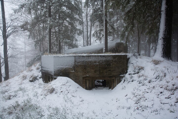 Pair of concrete bunkers in snowy forest covered with fog. Orlicke hory, Czechia.