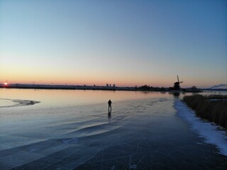 Silhouetted figure is walking across a frozen lake illuminated by the setting sun