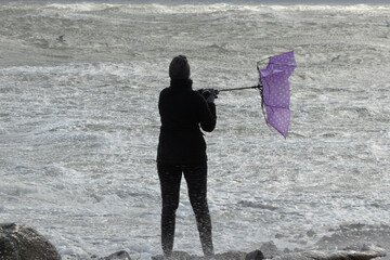 Frau mit Schirm am Meer bei einem Orkan, Unwetter, Sturmtief, Extremwetter