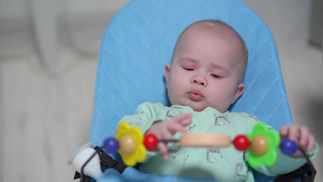 Newborn baby swings in a chaise longue and looks at hanging toys