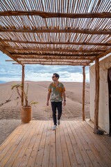 Fototapeta premium Man with sunglasses walks on a wooden deck in a desert setting. Agafay desert, Morocco.