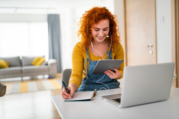 Relaxed, enthusiastic young college girl multitasking. Smiling woman writing in her notebook while...