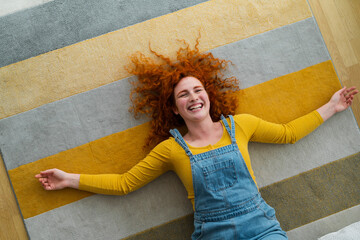 Happy young woman wearing bright colors, lying on the carpet, smiling and feeling a freedom while...