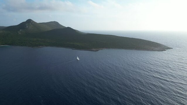 Aerial approach of white sailboat passing an island in Methoni, Greece in the Mediterranean Sea