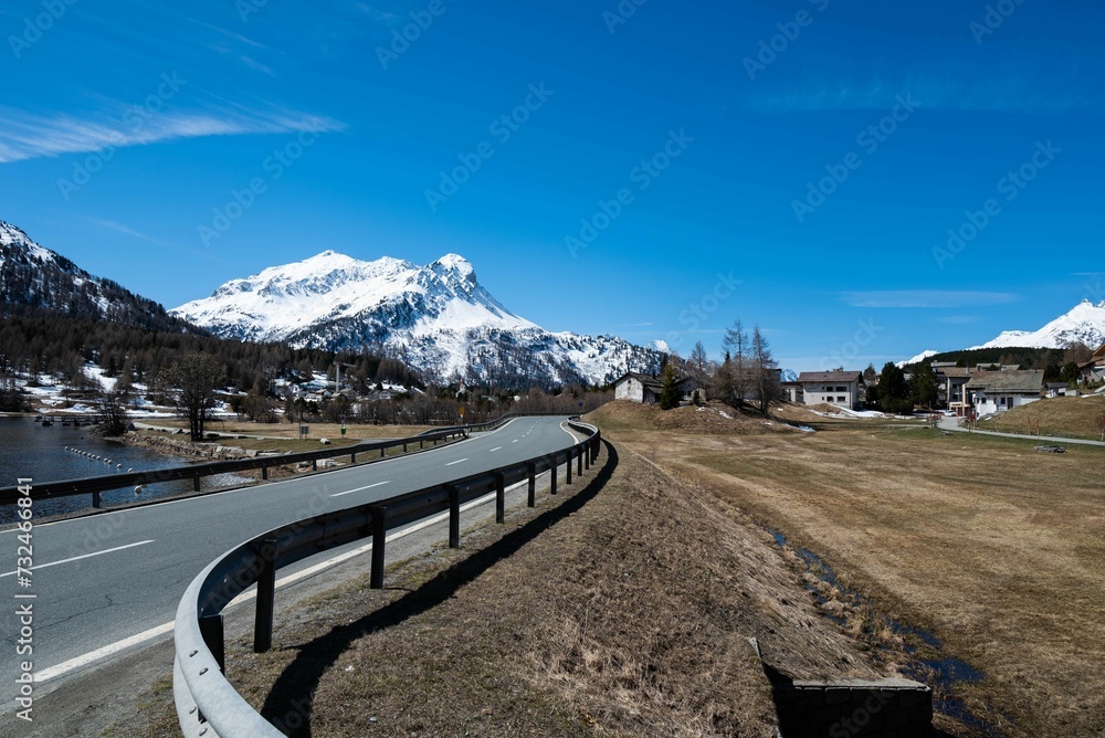 Wall mural a curve road passes by a mountain with some snow capped peaks