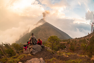 two people sitting on a large rock in the air with a view of the volcano