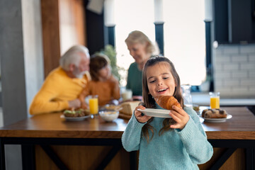 Smiling child at breakfast. Food and happy kids. The girl is eating a croissant. Cute preschool girl having a meal in the kitchen.
