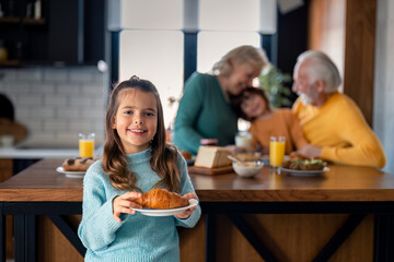 Portrait of cute preschool girl having a croissant for breakfast at grandparents house.