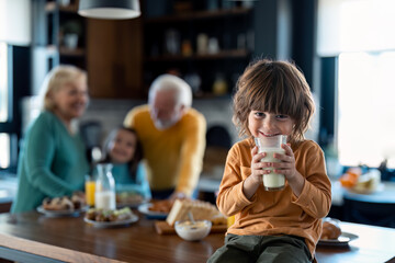 Adorable boy smiling at camera while having a glass of milk or yogurt for breakfast at grandparents home.