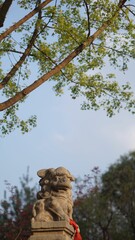 Fototapeta premium Weathered Asian stone statue resting atop a pedestal in a green, wooded area with trees