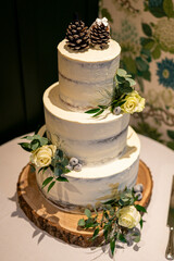 Elegant Three-Tier Rustic Wedding Cake with Pine Cones and Yellow Roses on a Wooden Stand