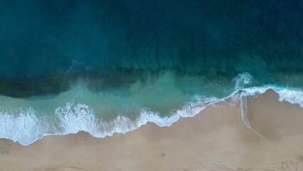 Aerial view of sea waves crashing against a beach in the daylight - Powered by Adobe