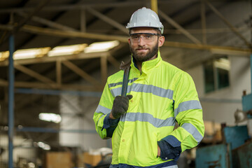 Portrait of caucasian industrial worker beard man with helmet crossed arms holding wrench in industry factory . confidence labor male Engineer standing in manufacturing.