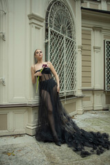 a young girl of about 30, of European appearance, in a chic designer black tulle dress near a beautiful building in nature with flowers and calla lilies in her hands. Photo shoot, stylish look