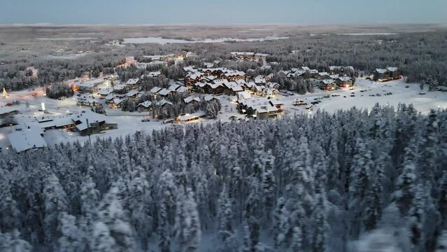 Aerial view of snowy forest trees and illuminating house in the evening in Levi village, Finland