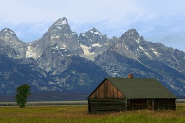 Fototapeta na wymiar Closeup of a wooden hut in a lush green with a great mountain rage in the background Great Teton