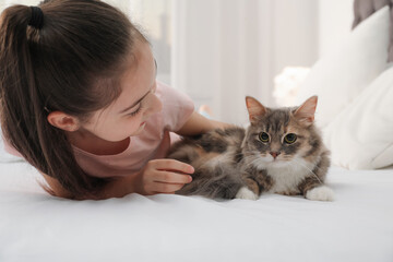 Cute little girl with cat lying on bed at home. First pet