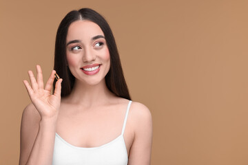 Beautiful young woman with vitamin pill on beige background. Space for text