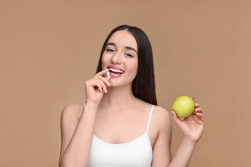 Beautiful young woman with vitamin pill and apple on beige background