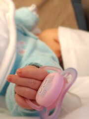 Vertical closeup of a pacifier on the hand of a cute, sleeping newborn
