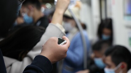 Person looking at his phone with people in the background riding in a subway with face masks on